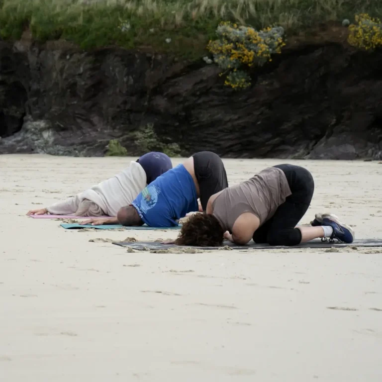 a group of three adults doing a yoga pose on the beach